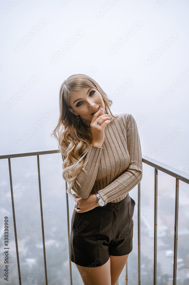 Blonde on the balcony in a sweater. Fog over the city