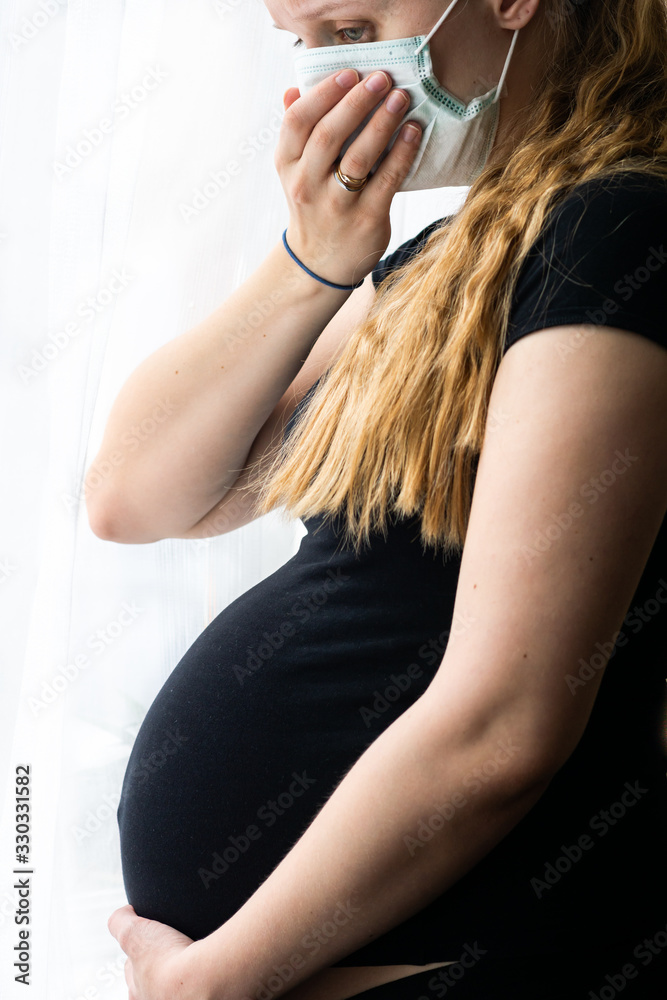 Pregnant caucasian woman coughing, wearing preventive mask, worrying about her unborn baby during coronavirus pandemic in Europe. Home quarantine of sick pregnant woman, trying to avoid contamination. Pregnant caucasian woman coughing, wearing preventive mask, worrying about her unborn baby during coronavirus pandemic in Europe. Home quarantine of sick pregnant woman, trying to avoid contamination.