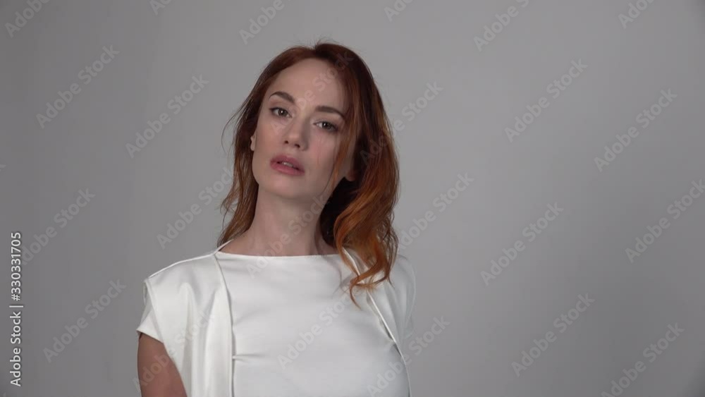 Nice young redhead woman posing for camera on neutral background. turns sharply and waves his hair. Shrewdly looking at the viewer Nice young redhead woman posing for camera on neutral background. turns sharply and waves his hair. Shrewdly looking at the viewer