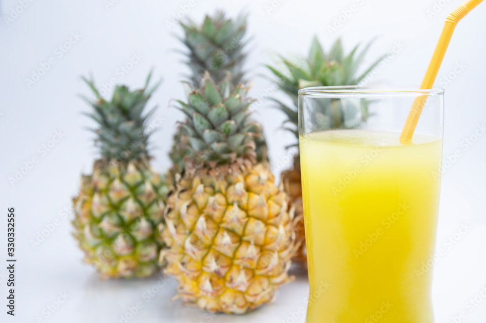 The yellow pineapple juice is appetizing in a glass and has a yellow tube. Four pineapples placed behind and white background. The yellow pineapple juice is appetizing in a glass and has a yellow tube. Four pineapples placed behind and white background.