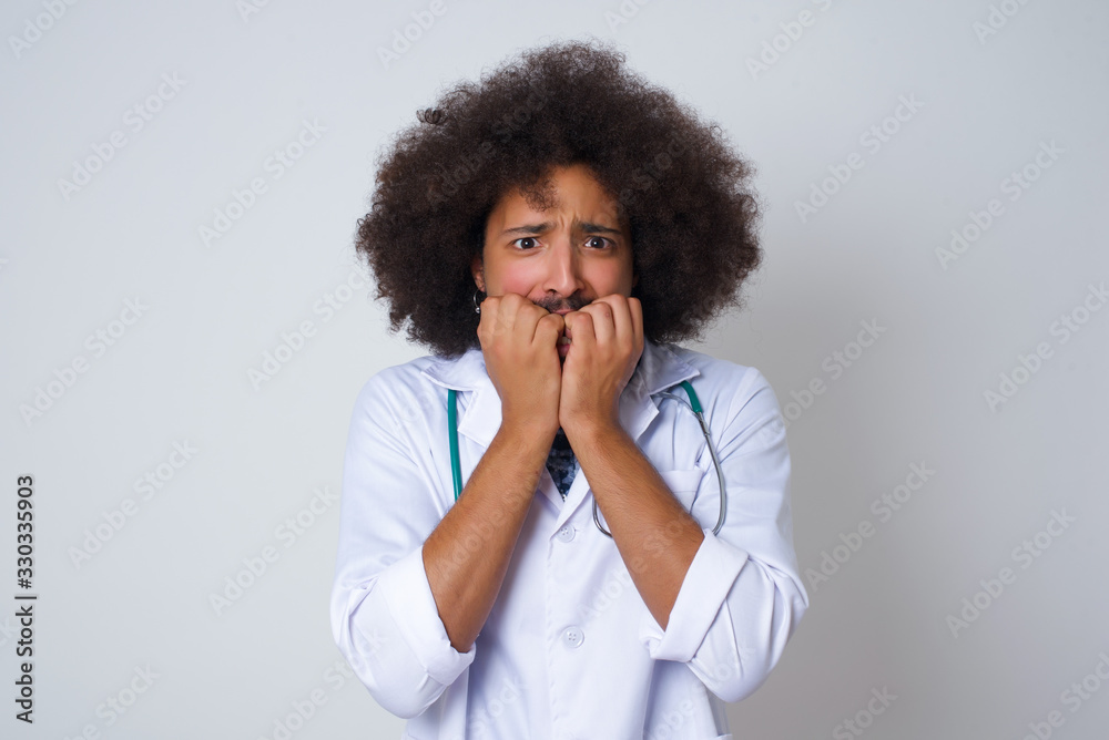 Anxiety. African American doctor man covering her mouth with her hands and standing indoors. Scared from something or someone bitting nails. Anxiety. African American doctor man covering her mouth with her hands and standing indoors. Scared from something or someone bitting nails.