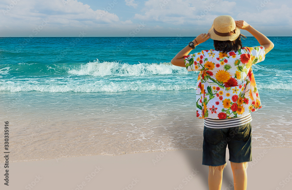 Woman looking at sea and holding straw hat on head