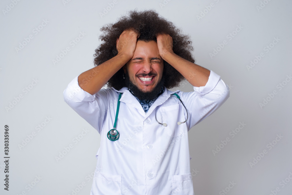 African American doctor man wearing medical keeps hands on temples, feels strong headache, closes eyes with pain, need healthy sleep, being overworked, fatigue and tired. African American doctor man wearing medical keeps hands on temples, feels strong headache, closes eyes with pain, need healthy sleep, being overworked, fatigue and tired.