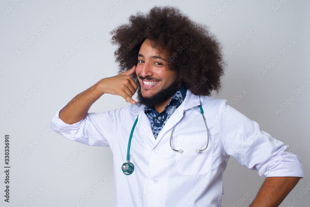 Attractive young doctor male in casual clothes imitates telephone conversation, keeps hand near ear as if holding mobile phone, has confident facial expression, isolated outdoors. Call me! Attractive young doctor male in casual clothes imitates telephone conversation, keeps hand near ear as if holding mobile phone, has confident facial expression, isolated outdoors. Call me!