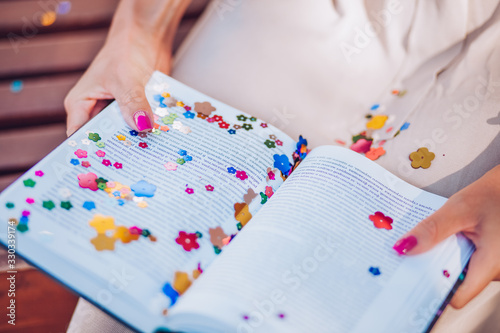 A woman's hands hold a book covered with colourful sequins