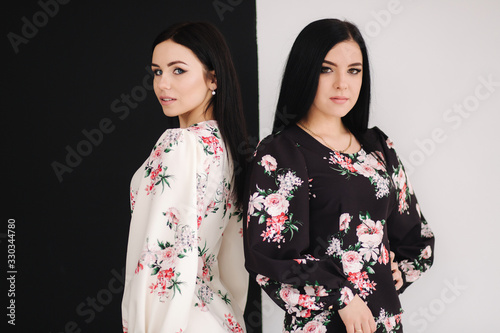 Two fashion brunette models in spring dresses posing in the studio. Black and white background © Aleksandr