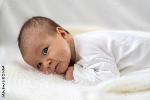 A 3 week old Caucasian baby girl smiles as he lays on a fluffy down duvet comforter on a bed