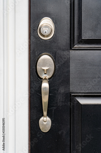 Close-up view of brand new nickel single cylinder front door handle set and matching lock deadbolt  on a black wooden door