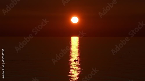 Una barca de pescadores navega a remo sobre la estela dorada intensa de una puesta de sol en el Mediterráneo, al sur de España