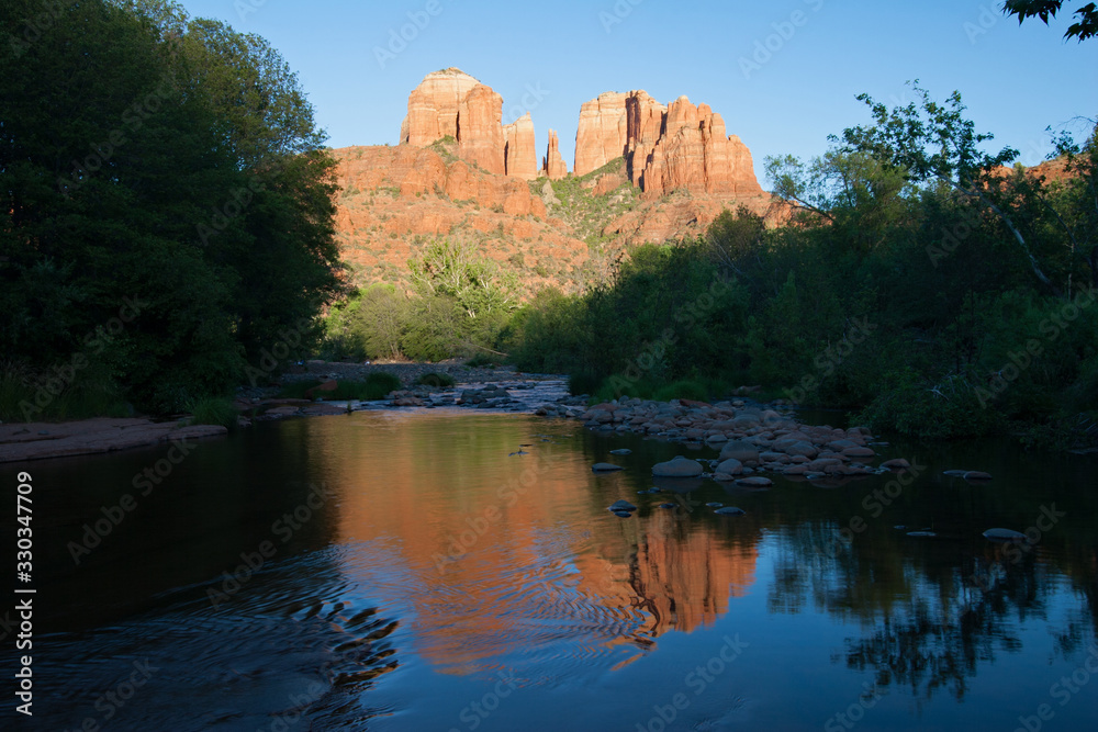 Fototapeta premium Cathedral Rock reflected in Oak Creek amidst green summer foliage near Sedona, Arizona on cloudless late summer afternoon.