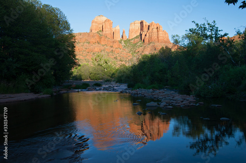 Cathedral Rock reflected in Oak Creek amidst green summer foliage near Sedona  Arizona on cloudless late summer afternoon.