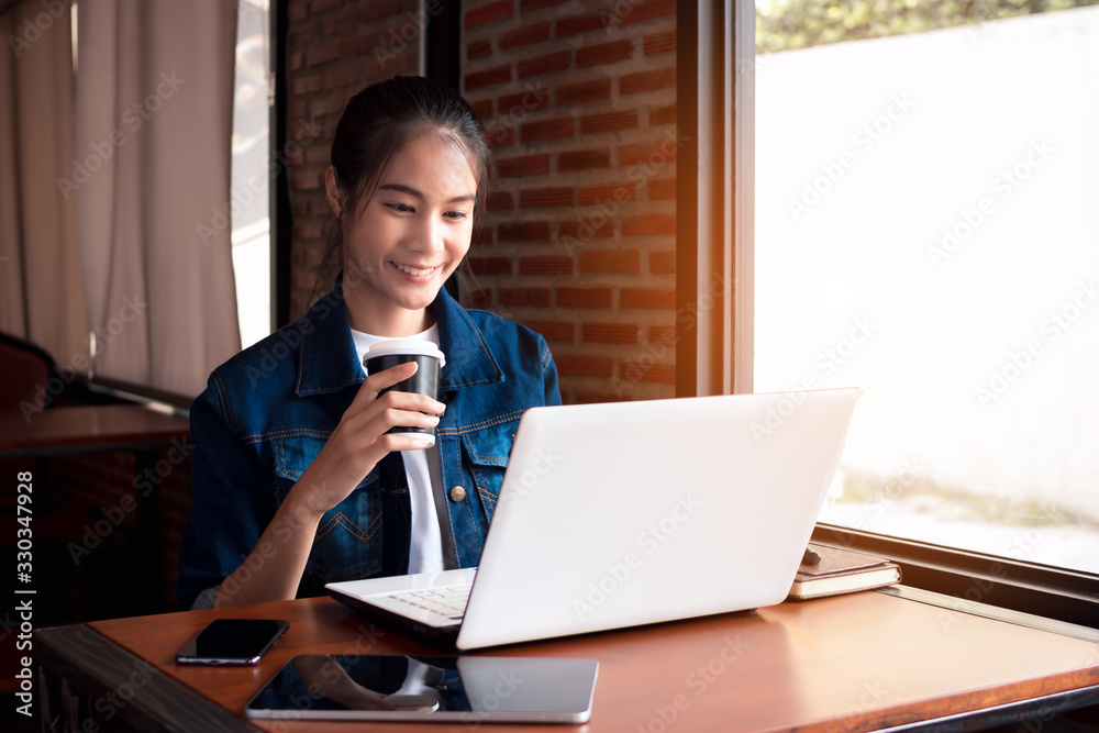 Young woman holding hot coffee cup with use laptop doing work.