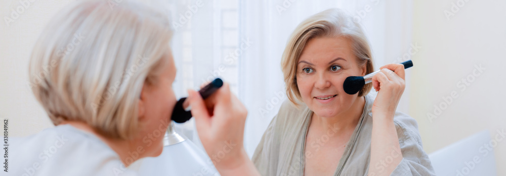 Portrait beautiful old woman touching her perfect skin looking mirror. Close- up Mature woman's face with brush touching skin of her face. Portrait beautiful old woman touching her perfect skin looking mirror. Close- up Mature woman's face with brush touching skin of her face.