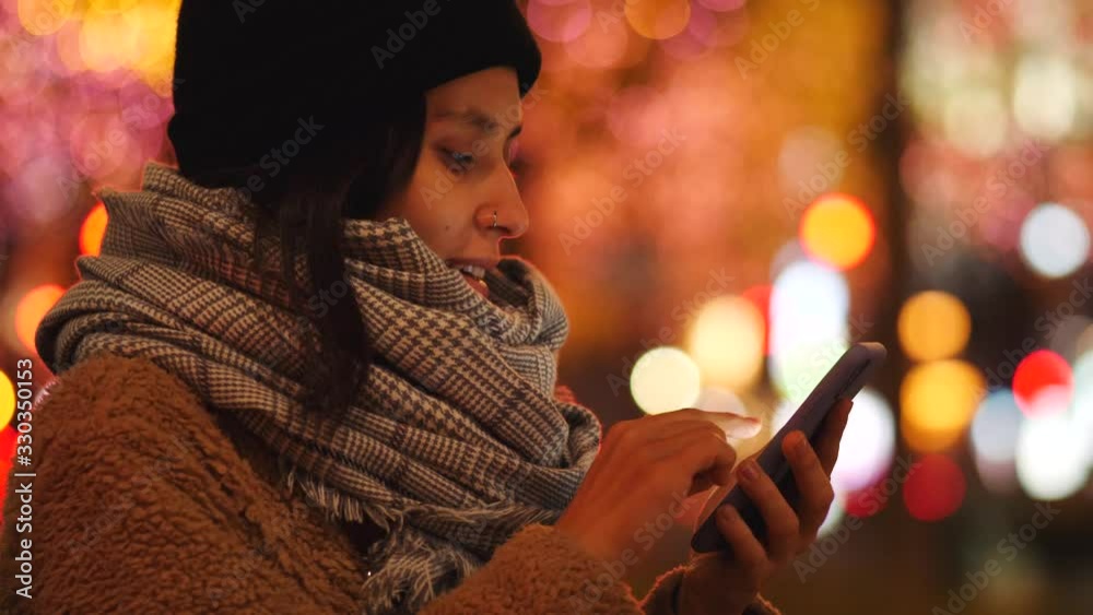 Young Mixed Race Woman Using Smartphone And Smiling In The Evening Lights. 4K Slow Motion Footage. Young Mixed Race Woman Using Smartphone And Smiling In The Evening Lights. 4K Slow Motion Footage.