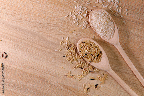 Abstract colorful food background. Texture of rice grains of different colors. Top view on two wooden spoons with white and brown grains of rice close-up. Horizontal, free space on the left, flat lay.