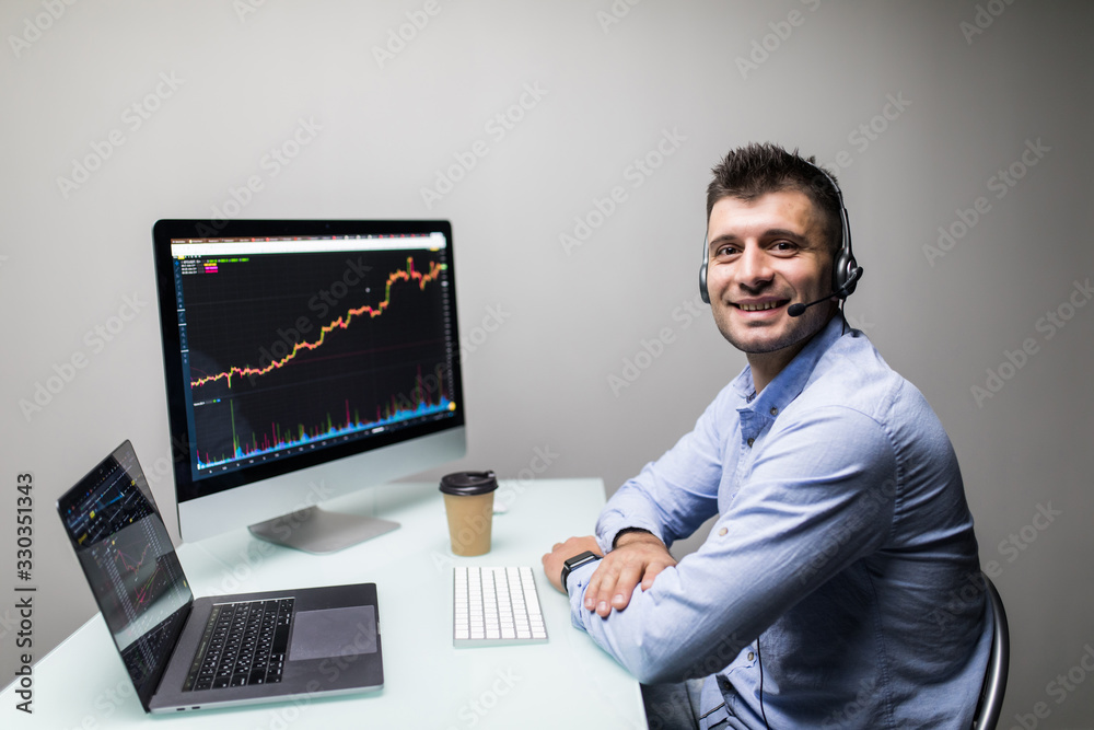 Side view of male trader with coffee cup using multiple computer screens while communicating through headphones at desk Side view of male trader with coffee cup using multiple computer screens while communicating through headphones at desk