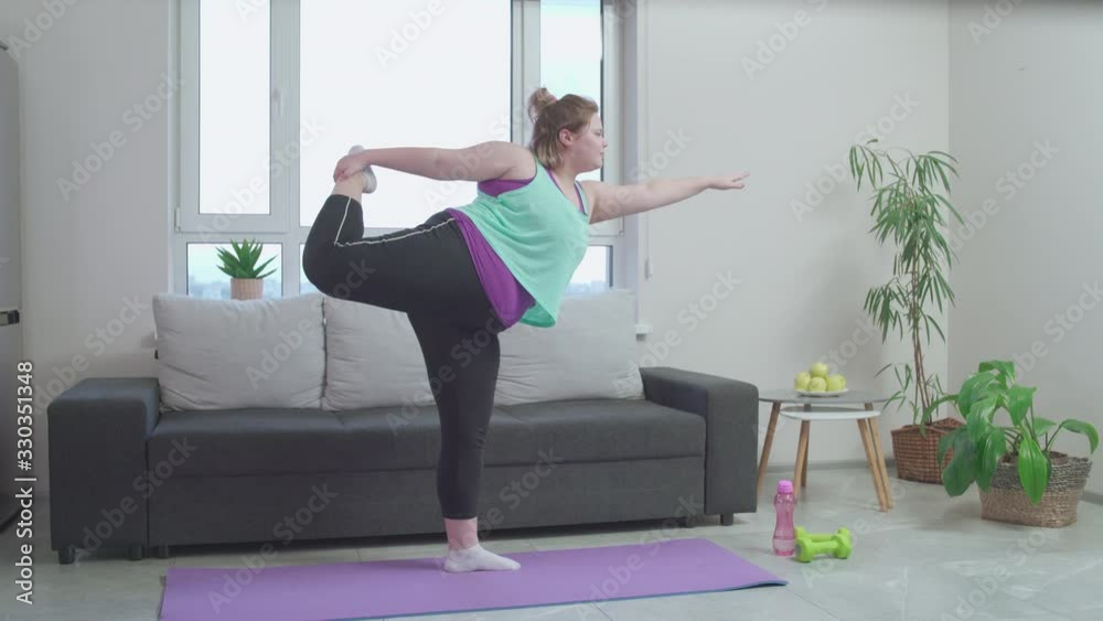 Clumsy plus size girl doing yoga exercise home, working out to be fit and slim