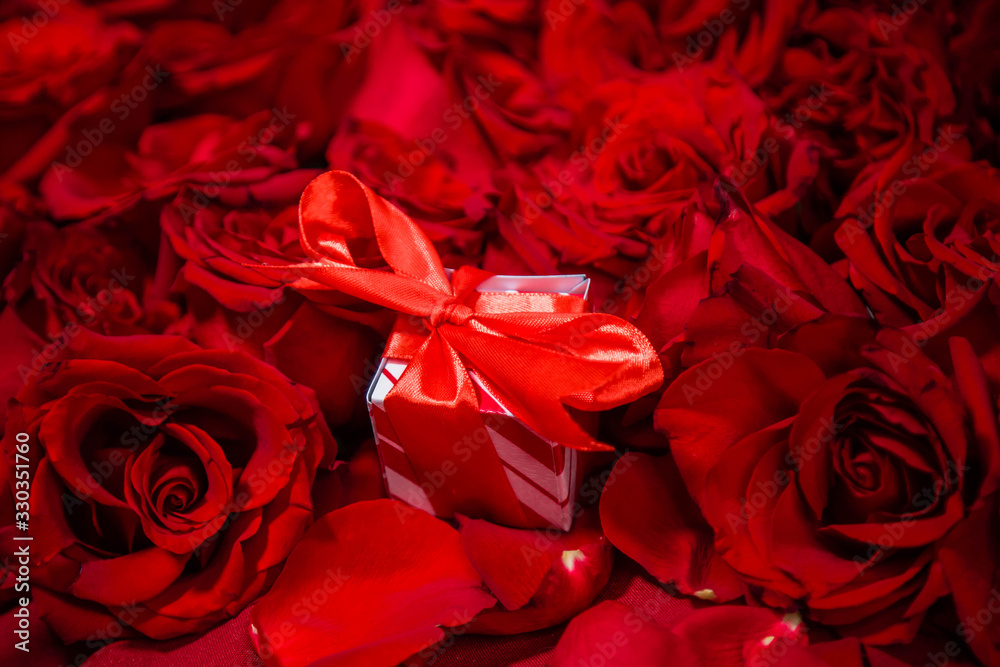 Naklejka premium A gift box with a red bow lies in red roses.