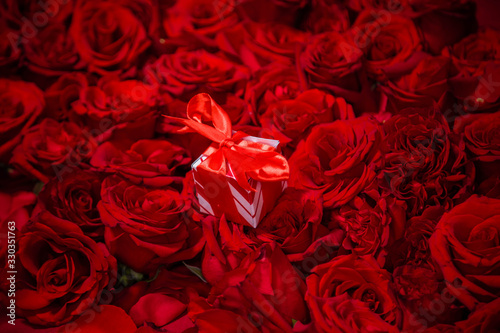 A gift box with a red bow lies in red roses.
