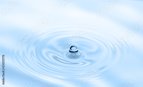 Water drop falling into water making splash and ripples. Light blue nature background.