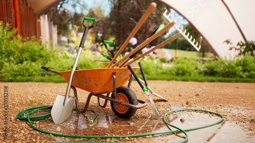 Garden tools gathered around a wheelbarrow in a beautiful, lush garden. 4KHD photo