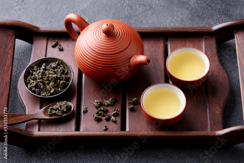 Green tea oolong in teapot and chawan bowls, cups on a wooden tray. Grey background. Close up. photo