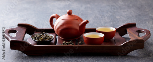 Green tea oolong in teapot and chawan bowls, cups on a wooden tray. Grey background.
