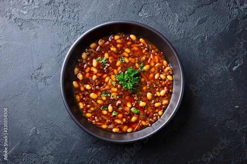 Bean soup in a black bowl. Dark background. Close up. Top view.
