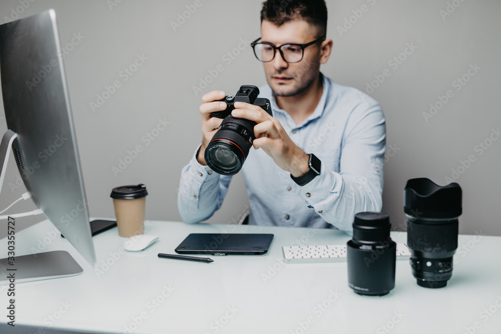 Man photographer watching at camera while holding it in arms in office. Man photographer watching at camera while holding it in arms in office.