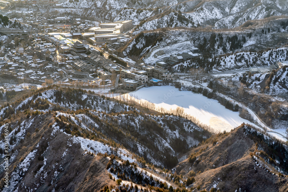 Obraz premium The view on the top of the mountain is covered with snow, below is the city with a frozen lake.
