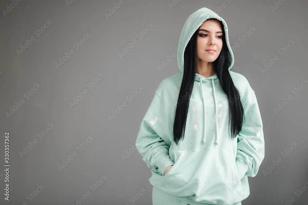 Attractive young model in tracksuit. Woman demonstrating clothes in studio. Gray background Attractive young model in tracksuit. Woman demonstrating clothes in studio. Gray background