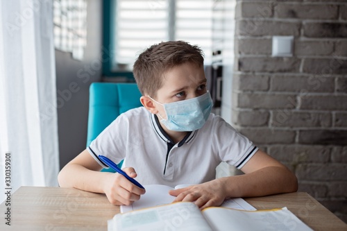 Child in protective medical mask doing his homework. School closed during coronavirus