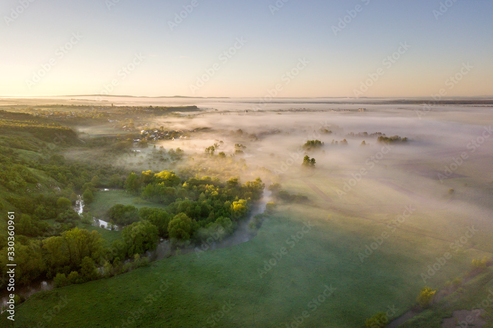 Top view of green cultivated hills and green trees in foggy valley. Spring misty landscape panorama at dawn.