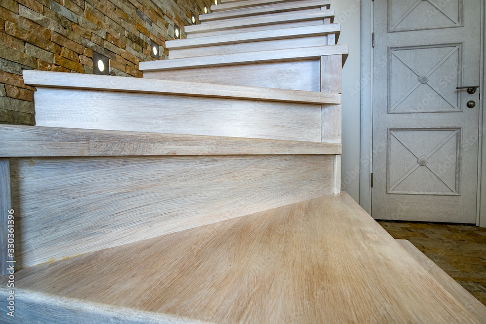 Stylish wooden contemporary staircase inside loft house interior. Modern hallway with decorative limestone brick walls and white oak stairs. Stylish wooden contemporary staircase inside loft house interior. Modern hallway with decorative limestone brick walls and white oak stairs.