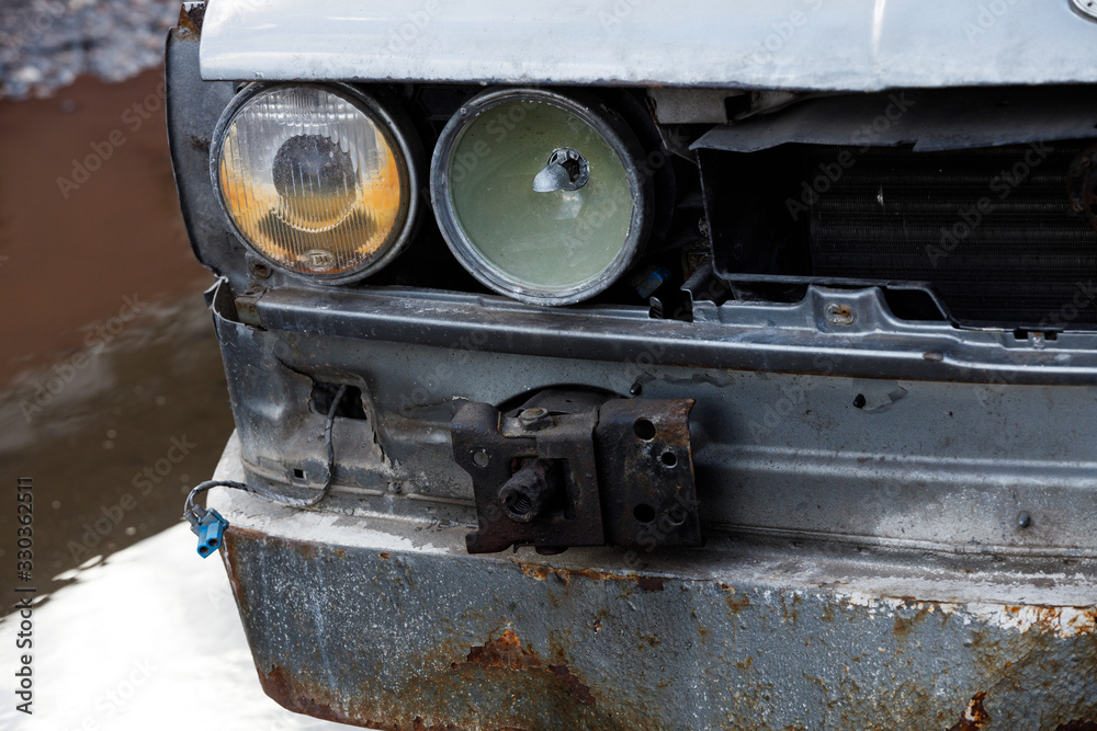 Detail of a wrecked blue car. Broken bumper car under the front lamp