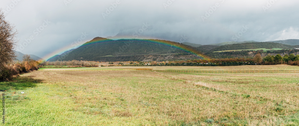 Obraz premium View of a rainbow coming out, in a valley with the mountains in the background.