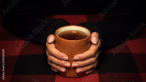 The girl is holding a Cup of tea on a blanket