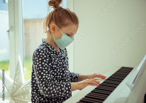 Little child girl playing piano with maskat quarantine because of coronavirus photo