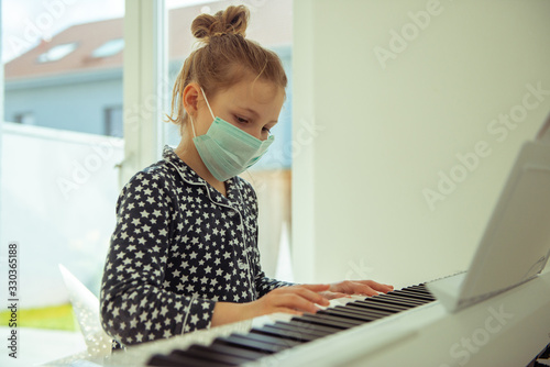 Little child girl playing piano with maskat quarantine because of coronavirus