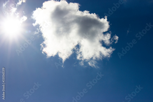 White cloud and bright sun against blue sky background.