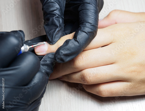 A manicurist, wearing black gloves, does hardware manicure. Cosmetology, hand care, manicure, finger nail care