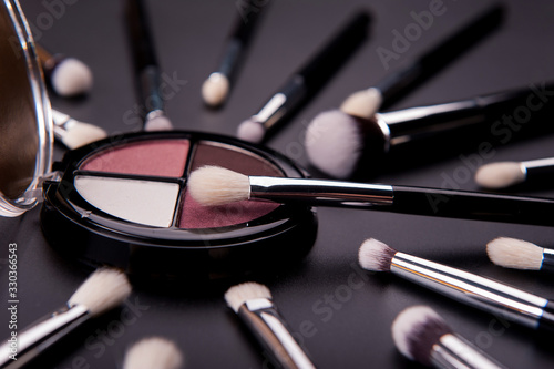 Cosmetic palette and face shadow with brushes lies on a black background