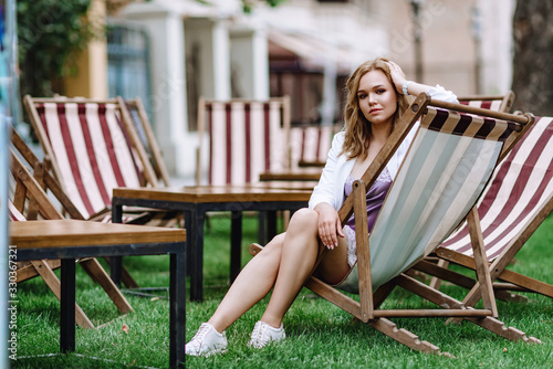 beautiful girl in a white jacket in the city. blonde woman posing. sitting on a chair