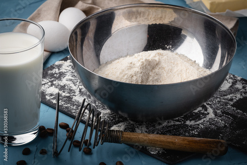 Flour in a steel bowl, a glass of milk and eggs