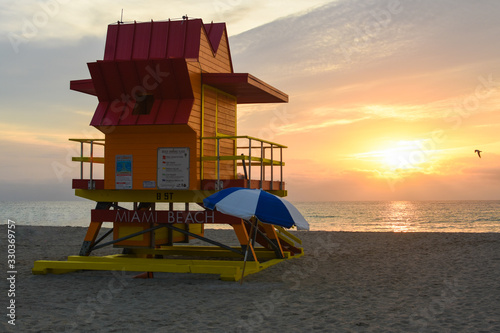 Sun rising on Miami Beach in front of an orange lifeguard hut with a silhouette of a seagull flying by © Joshua Sands Photo