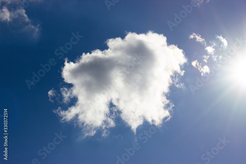 White cloud and bright sun against blue sky background. © malshak_off