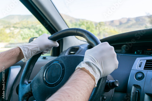Hands holding the steering wheel of a car while driving with latex gloves to avoid contagion
