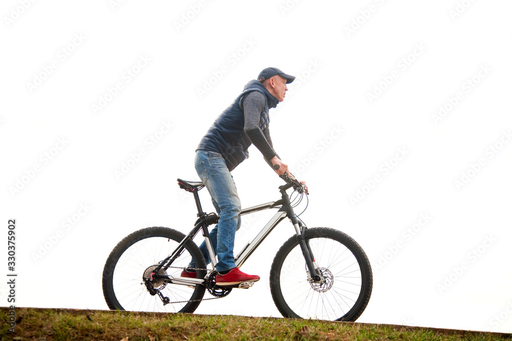 Naklejka premium the young man goes by bicycle against the background of the white sky in the park