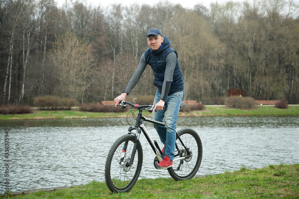 Obraz premium the young man goes by bicycle in the park in the spring