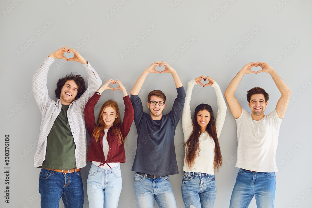 Obraz premium Group of friends making a heart with hands smiling while standing on gray background.